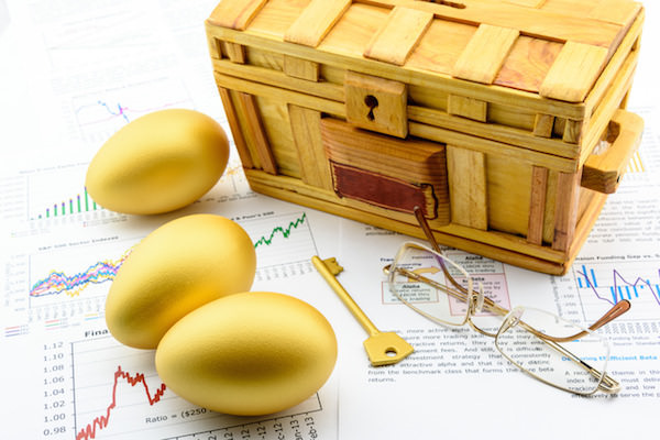 Three golden eggs and a golden key with a wooden chest on business and financial reports.